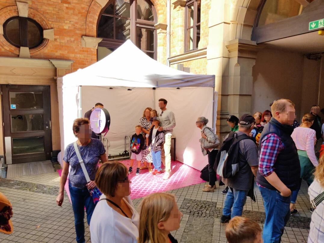 Fotobox auf dem Stadtfest am Rathaus Wiesbaden Eine Familie posiert für ein Foto in einer Fotobox, die unter einem weißen Zelt auf dem Stadtfest Wiesbaden am Rathaus aufgestellt ist. Im Vordergrund warten weitere Besucher in einer Schlange, um ebenfalls ein Foto zu machen.