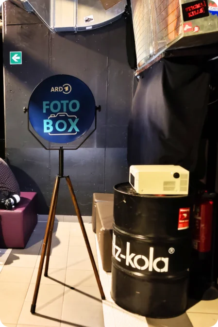 Fotobox-Setup mit WLAN-Verbindung im Club Keller Ein Mann sitzt neben einer Fotobox, die für eine Party in einem Club aufgestellt wurde. Im Hintergrund sind Bildschirme zu sehen, während eine Wi-Fi-Verbindung den kabellosen Druck ermöglicht.