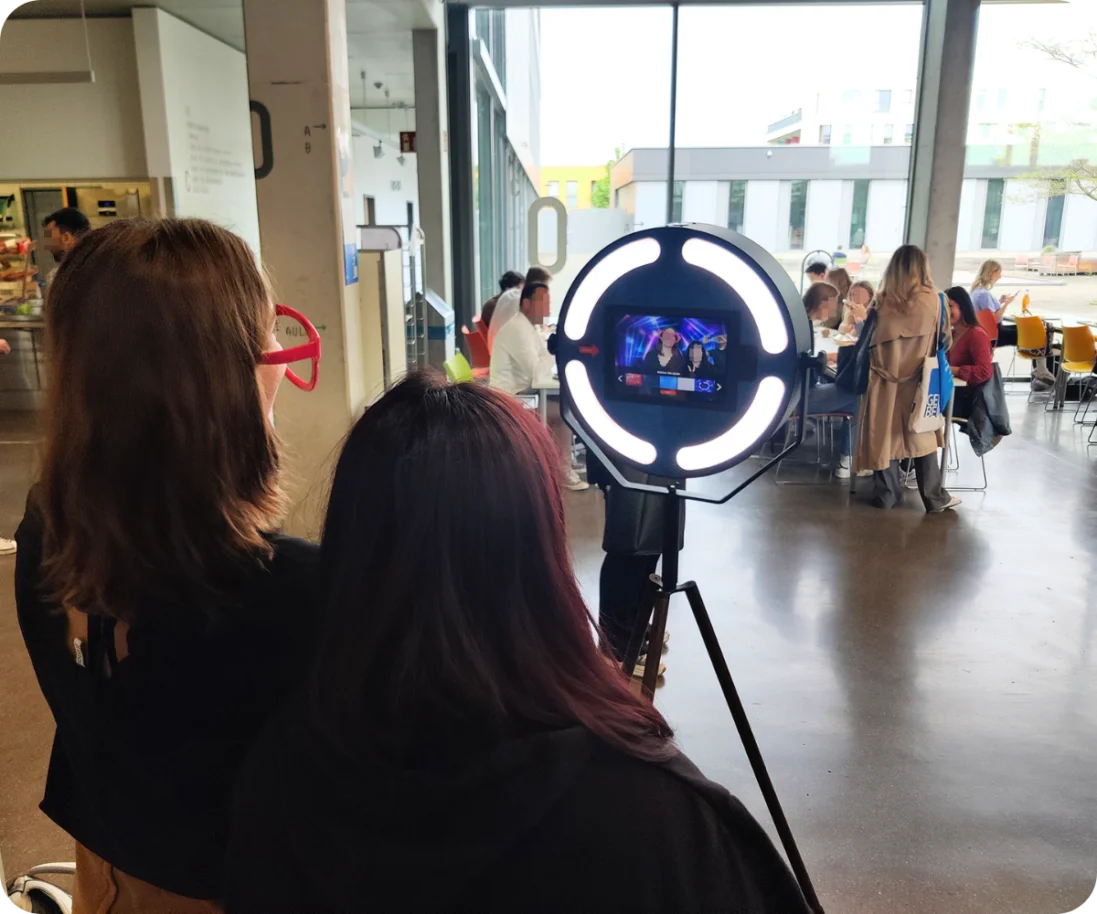 Fotobox-Spaß auf den Unternehmertagen der Hochschule Mainz Zwei Besucherinnen posieren für ein Foto an einer Fotobox auf einem Event im Inneren der Hochschule Mainz. Im Hintergrund sind weitere Besucher und Tische in einem großen, hellen Raum zu sehen.