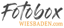 Das Logo der Firma Fotobox Wiesbaden. Der Schriftzug "Fotobox" ist in einem stilisierten dunkelgrauen Design, darunter der Slogan "Wiesbaden" in Orange.